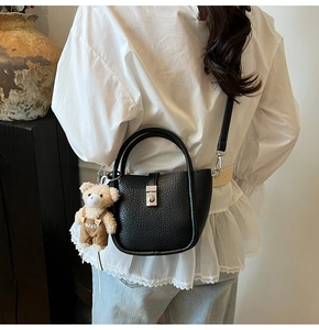 Détail du sac seau en cuir noir avec fermoir rotatif argenté et charmant ours en peluche