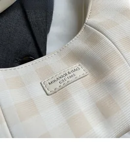 Detailed close-up of beige plaid handbag featuring a leather label with precise stitching