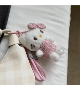 Close-up of Hello Kitty plush charm in pink tweed dress attached to beige plaid handbag