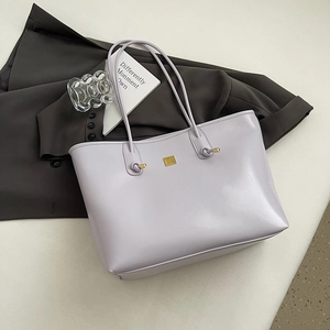 Detail of lavender glossy leather tote bag with gold logo plaque on grey suit