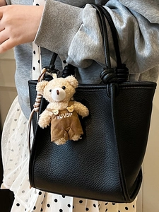 Sac à main noir épuré avec texture litchi et pendentif ours en peluche sur le modèle