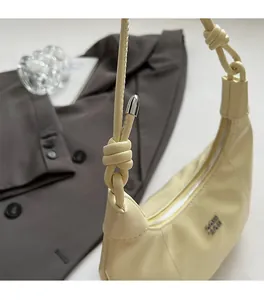 Nahaufnahme des Knotenschultergurts und silbernen Logos auf cremefarbener Tasche