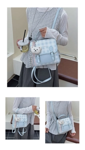 Close-up of light blue plaid handbag with double buckles and a cute plush bear charm