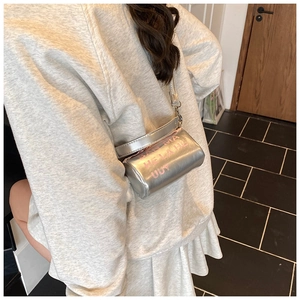 Détail du sac cylindrique argenté avec texte Y2K rose porté à l'épaule du mannequin