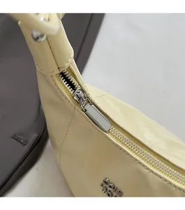 Detailansicht des silbernen Reißverschlusses und Metalllogos auf der beigen Handtasche