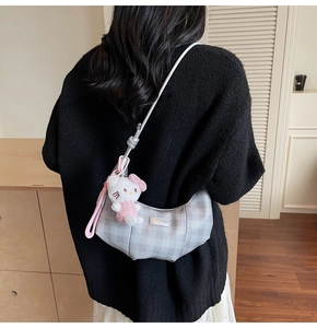Detail of silver checkered crescent bag with a plush character charm on shoulder