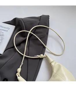 Nahaufnahme der cremefarbenen Lackledertasche mit dekorativem Knotengurt und Metallschnallen