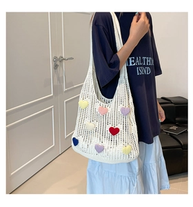 Detail of white crochet tote bag showing colorful knitted heart patches and hollow knit texture