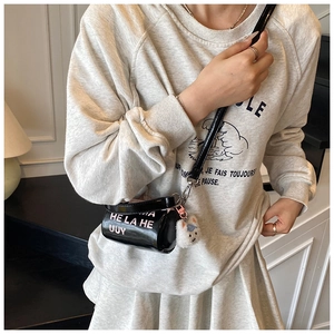 Détail du sac cylindrique noir brillant avec un joli pendentif en peluche blanche
