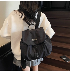 Detail of minimalist black nylon backpack with flap closure and decorative drawstrings