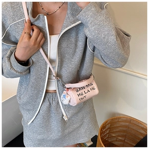 Gros plan détaillé d'un sac bandoulière cylindrique rose avec lettrage noir et pendentif