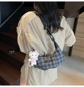 Close-up of a grey checkered crescent bag featuring a cute plush kitten charm on the strap