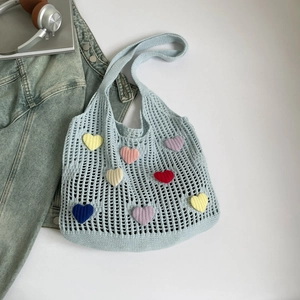 Detail of light blue knit tote bag featuring colorful crochet heart patches and hollow texture