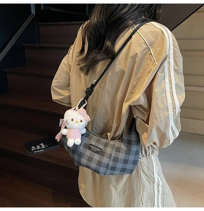 Detailed view of grey checkered shoulder bag with a cute plush charm on the strap