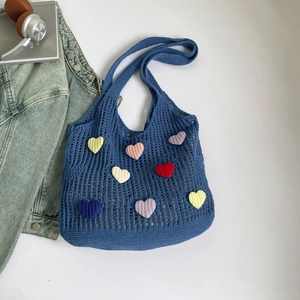 Detail of blue crochet tote bag featuring colorful heart patches and hollow knit design