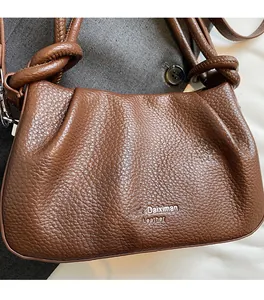 Detail of brown litchi pattern leather handbag featuring knotted strap and metal buckle