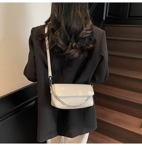 Detailed view of cream patent leather crossbody bag with silver chain on model's shoulder