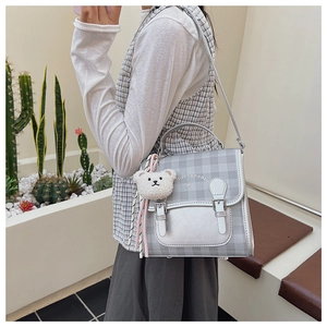 Detail showing grey plaid backpack with bow logo and a cute plush bear charm on side