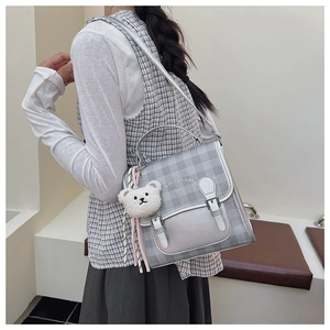 Detail of gray plaid messenger bag with a plush bear charm on a slim shoulder strap