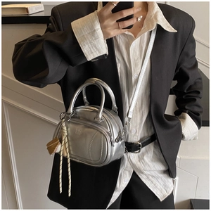 Detail of silver metallic boston bag featuring baseball charm and chic embossed texture