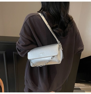 Close-up of silver cracked leather bag with metallic chain strap worn by a model