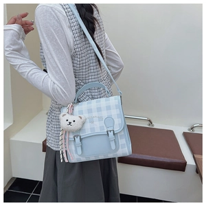 Detail view of the light blue checkered flap backpack with a cute white plush bear charm