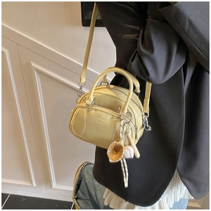 Close-up of a pale yellow baseball-inspired pillow bag with stitching and sports charms