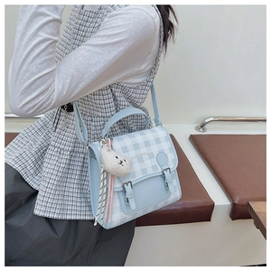 Close-up of blue plaid backpack with leather flap and cute plush bear charm detail
