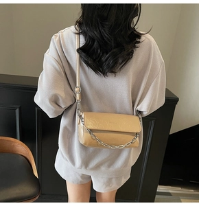 Detail of beige glossy leather crossbody bag with silver chain strap and logo