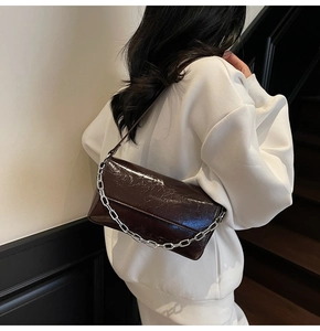Detail of dark brown glossy leather shoulder bag with a bold silver chain strap accent