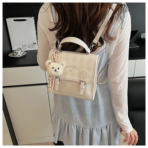 Close-up of cream plaid backpack with plush bear charm and bow detail on the cover