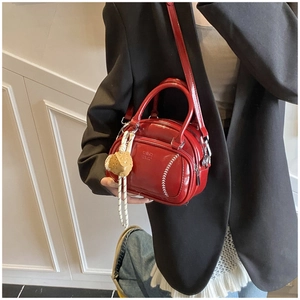 Detail of red patent leather pillow bag with baseball stitching and charms on a model