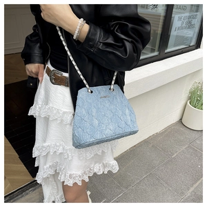 Street style view of light blue pleated shoulder bag with silver chain strap worn by a model