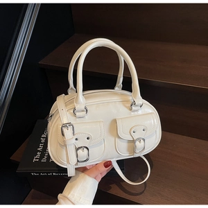 Detailed view of cream PU leather boston bag with silver buckles on dark wood steps