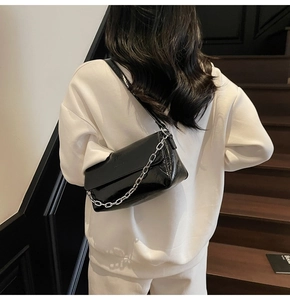 Detailed view of black patent leather baguette bag with silver chunky chain decoration