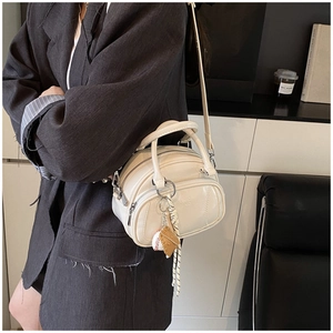 Close-up of cream white leather handbag with baseball charm and zip detail