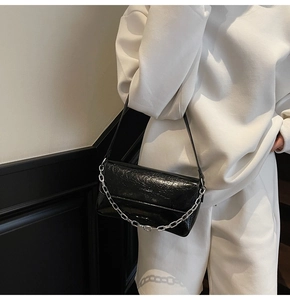 Detail of black patent leather baguette bag with silver chain strap on model's shoulder