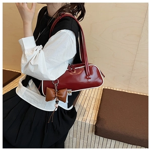 Détail d'un sac à bandoulière rouge foncé verni avec bordures blanches et nœud