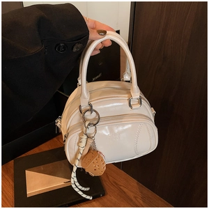 Detail of a creamy white multi-layer pillow bag with silver zippers and a woven charm
