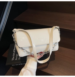Close-up of creamy white pleated baguette bag with silver chain strap on wooden stairs