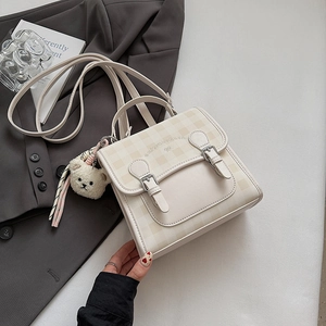 Detail showing the cream plaid pattern and decorative buckle straps of the mini backpack