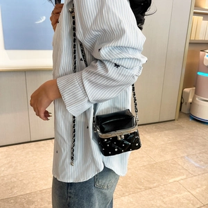 Detail of black quilted shoulder bag featuring metal kiss-lock and rivet accents