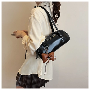 Vue détaillée du sac boston en cuir verni noir brillant avec breloque nœud marron foncé