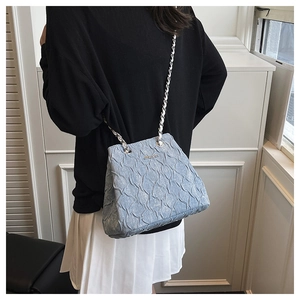 Detail of light blue pleated texture handbag with delicate chain strap and metal logo
