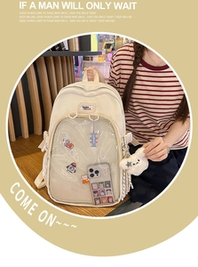 Detail of cream canvas student backpack featuring a transparent mesh front pocket and charms