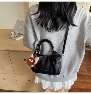 Detailed view of black pebbled leather handbag with gold logo and plush monster charm
