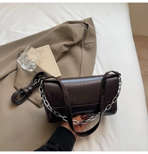 Detail of dark brown glossy leather baguette bag with silver chain and brand logo