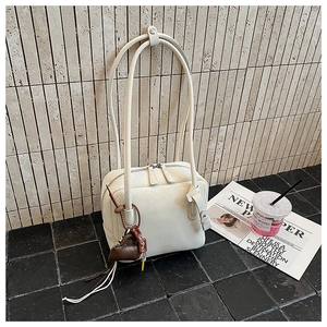 Close-up of cream white tote bag with dual zippers and heart tassel accessory