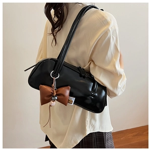 Sac baguette noir minimaliste avec charm nœud en cuir marron porté à l'épaule