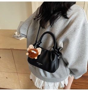 Detail of black pebbled leather crossbody bag with pleated texture and fuzzy monster charm